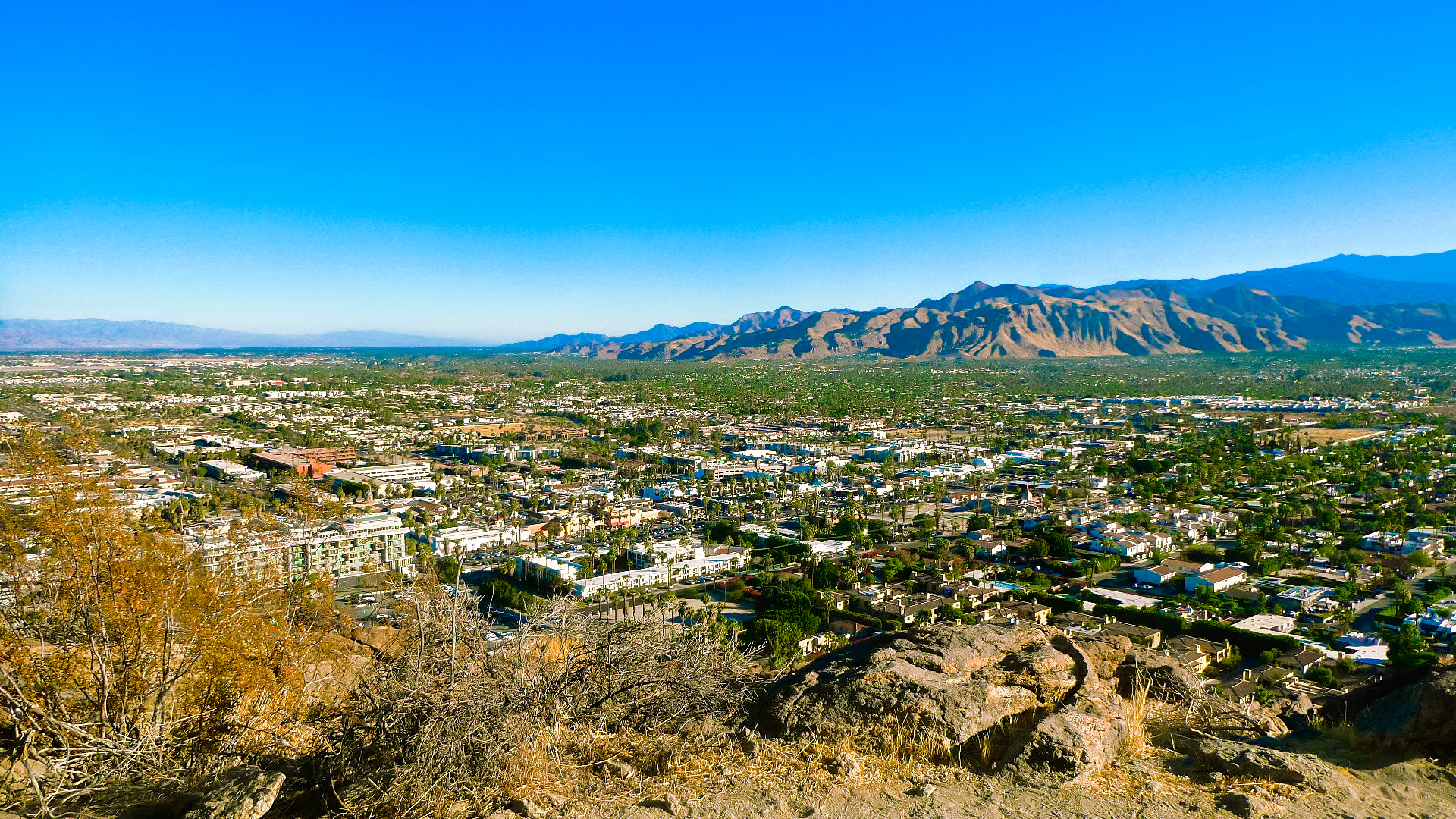 Stunning scenic vista view from high on a mountain trail where you can see forever, featuring Palm Springs and desert cities, that are embraced by a captivating and picturesque mountain range, all naturally gift wrapped under a crystal clear blue sky on a bright sunny day, that delivers the soothing and satisfying ambience of the serene desert landscape.