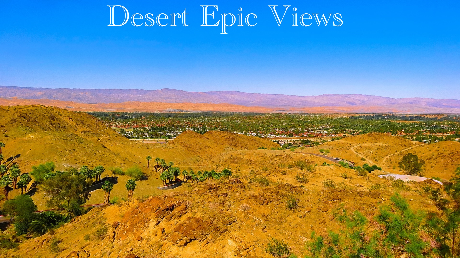 A truly breathtaking bird's eye view from the desert hills, offering a total panoramic experience that spans from the desert hills, across the desert floor, continuing over to the monumental mountain range, delivering a delightful desert dynasty time and place.